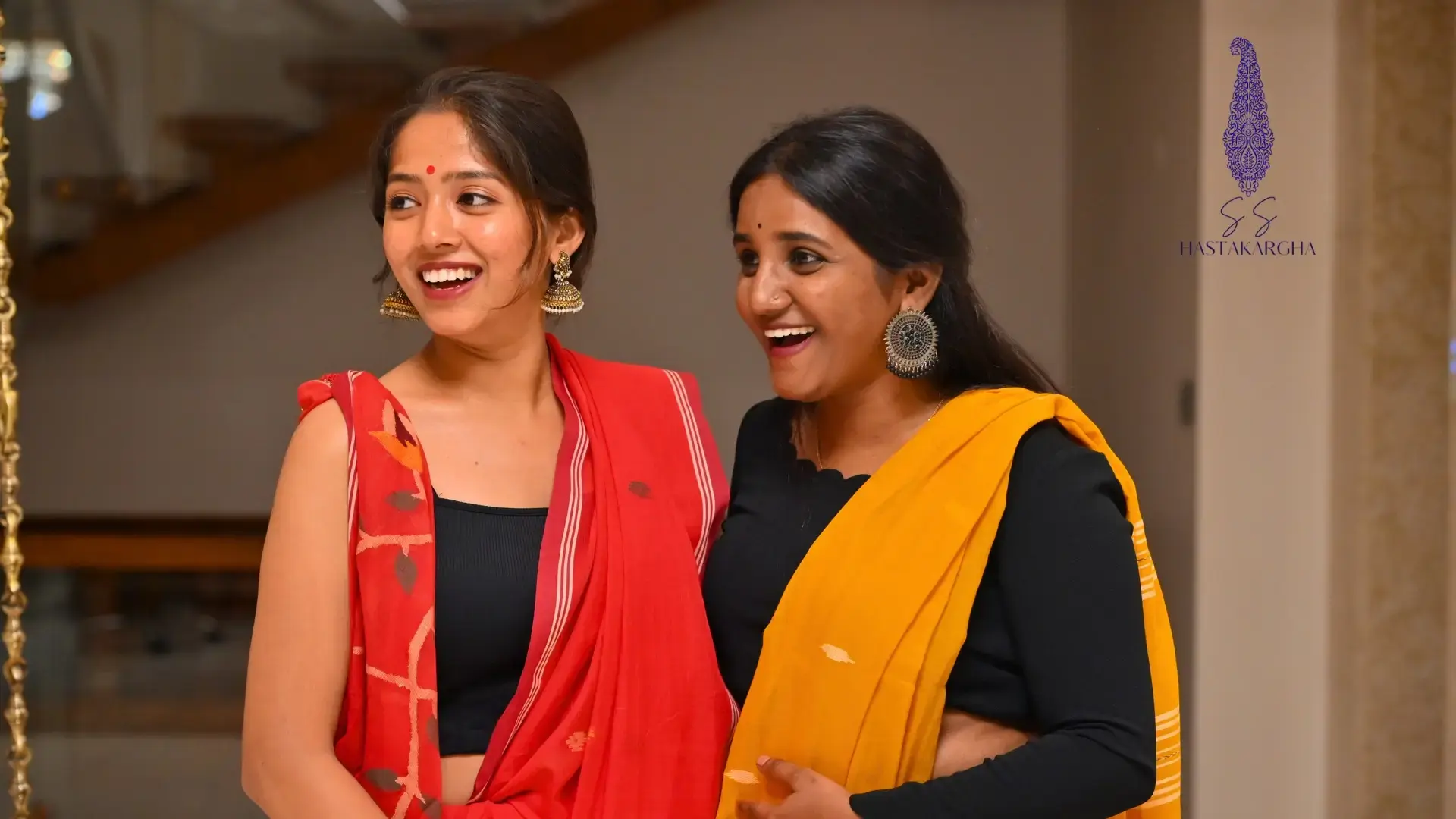 2 LADIES DRAPING THE SOFT PURE MAL JAMDANI SAREES IN RED AND YELLOW COLOURS REPRESENTING SINDOOR COMPLIMENTING HALDI